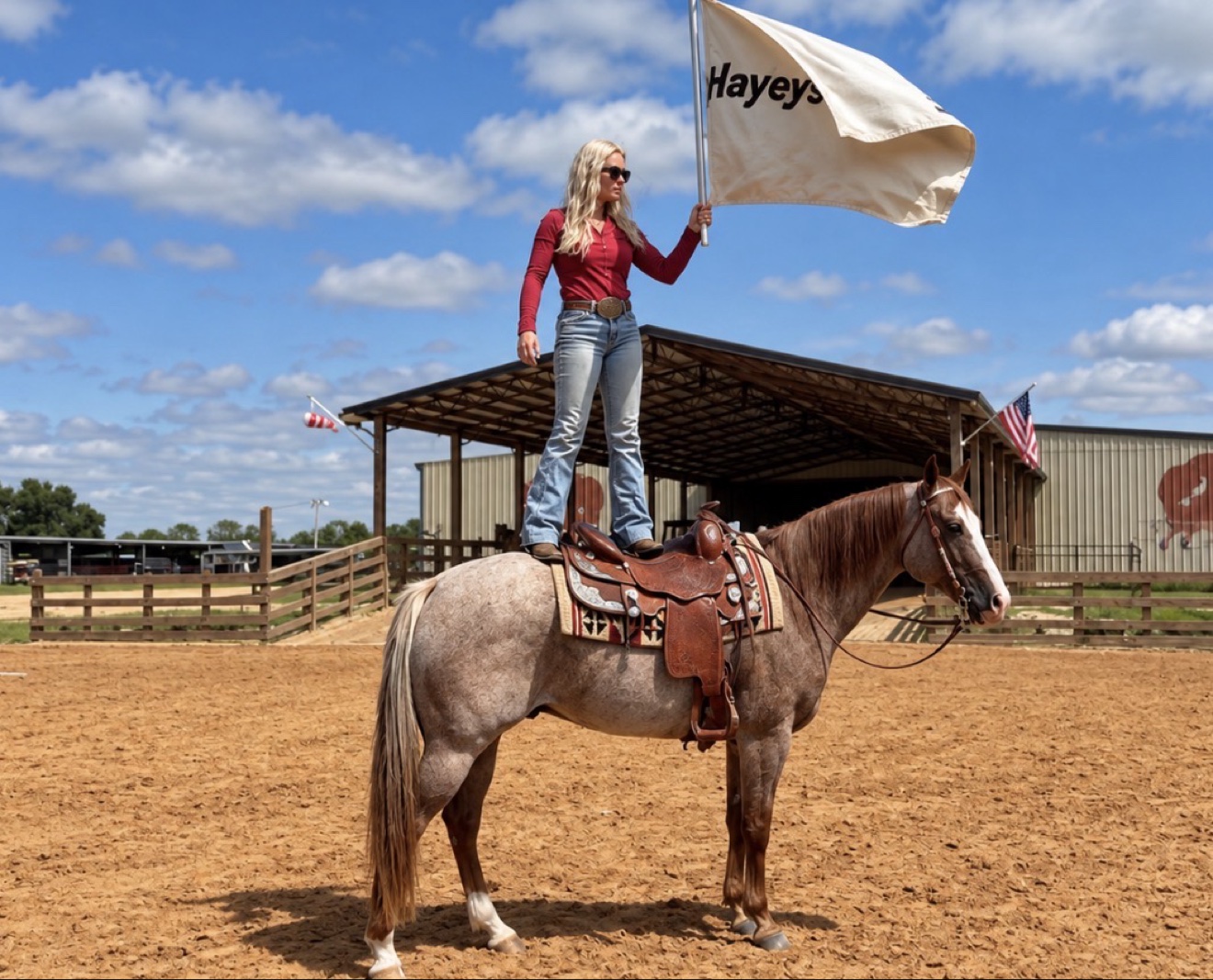 Hayley standing on Struttin Cowboy’s back with a flag near the barn